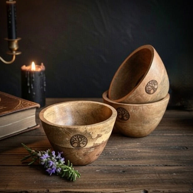 Three wooden smudge bowls with engraved treeb of life designs on a wooden surface with a candle and book in the background.