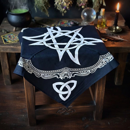 Triple moon and pentagram altar cloth on a small table with sorcery items behind