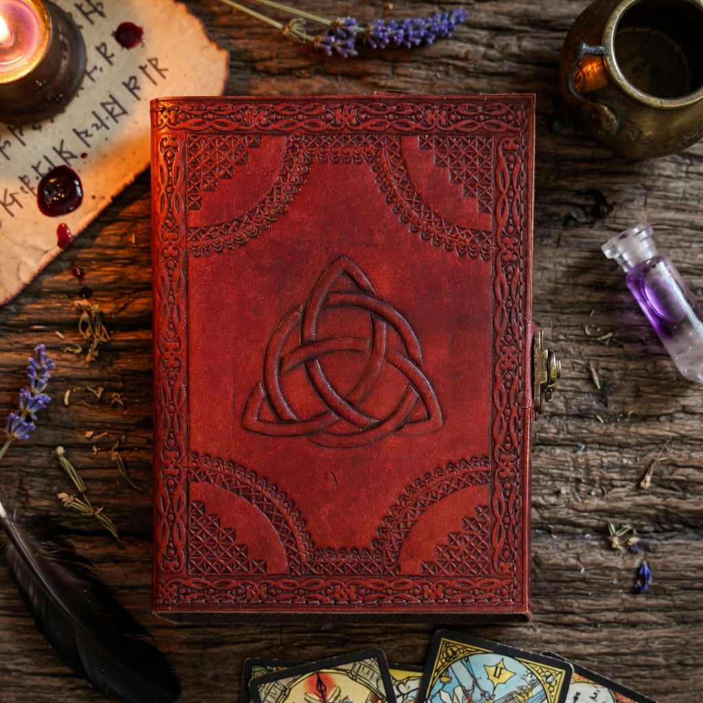 Embossed leather journal with Celtic knot design on a wooden surface with herbs and candles.