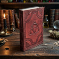 Leather book of shadows with Celtic triquetra design on a mystical table with candles and bottles.