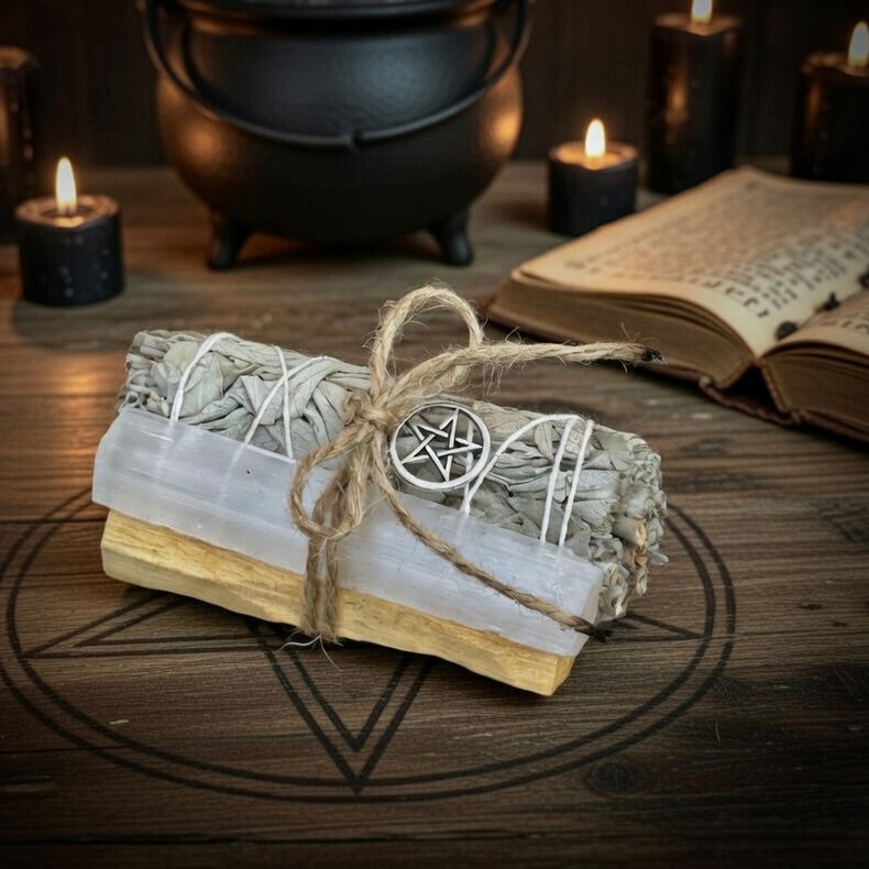 Bundled selenite, sage and palo santo sticks with a pentagram symbol next to a book and cauldron wooden surface.