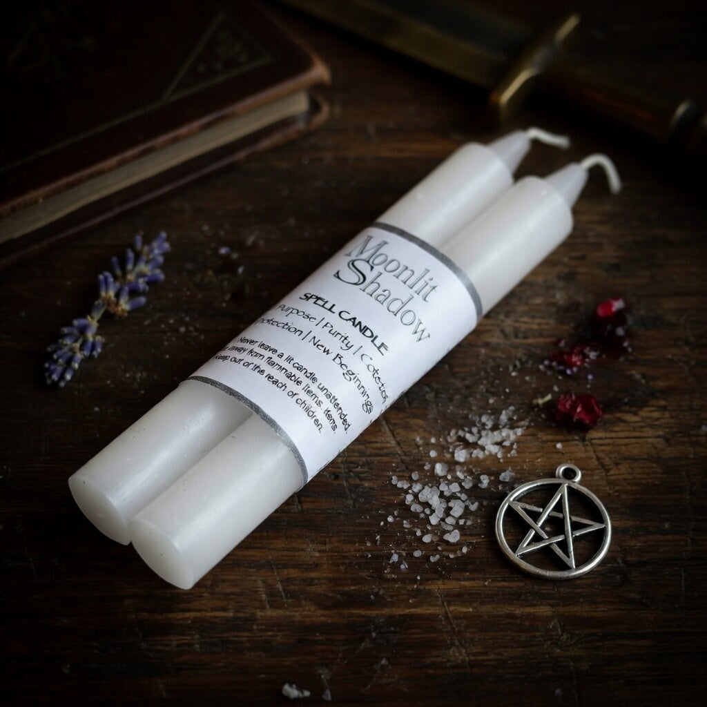 Two white spell candles labeled 'Moonlit Shadow' on a wooden surface with a pentagram pendant and lavender.